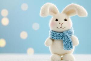 Fluffy white rabbit in blue scarf on snowy surface with pastel background creating a whimsical winter atmosphere photo