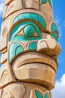 Intricately carved totem pole adorned with turquoise accents against a clear blue sky with soft clouds photo