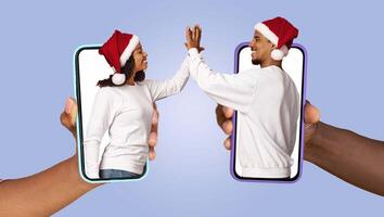 A married couple exchanges affectionate gestures through their smartphones while wearing festive holiday hats. They are engaged in a playful online interaction that showcases their connection. photo
