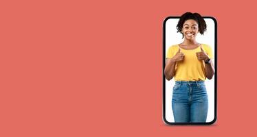 A person is smiling and giving a thumbs up gesture while interacting with a large smartphone. The background is a solid color, emphasizing their joyful expression and the technology. photo