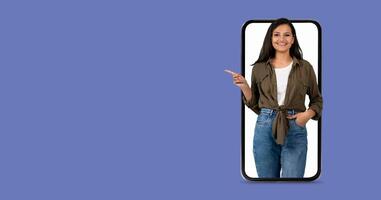 A woman with a friendly expression is interacting with a large smartphone. She points towards the screen while showcasing the engaging communication features of modern technology. photo
