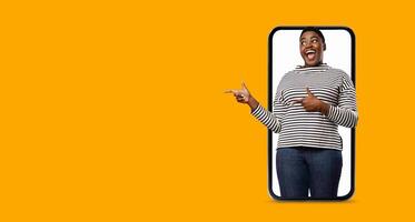 A person is playfully pointing while standing in front of a large smartphone display. The bright background enhances the cheerful communication, reflecting modern technology use. photo