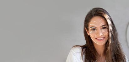 A woman is enjoying her skincare routine, smiling while applying products to her face. The setting is cozy, focusing on self-care and relaxation in a private space. photo