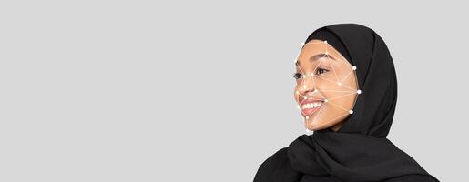 A woman in a black hijab smiles while facial recognition technology analyzes her features. The neutral background emphasizes the facial mapping points displayed on her face. photo