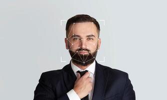 A suited man adjusts his tie as facial recognition technology highlights his features for identification purposes. The empty background emphasizes the focus on the subject's face and expression. photo