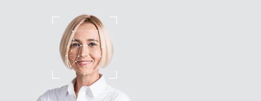 A person is engaged in facial recognition technology, smiling toward the camera against a blank background. The focus is on their facial features, illustrating identification processes. photo