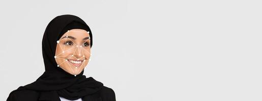This visual focuses on a woman wearing a hijab, smiling, as facial recognition technology highlights key facial features against a simple backdrop, emphasizing identification and technology. photo