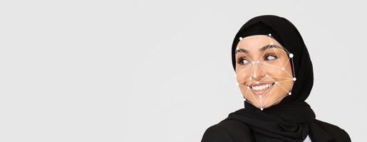 A woman in a hijab smiles against a plain background, while facial recognition technology highlights her features, illustrating advancements in identification methods. photo