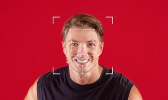 A man with a joyful expression is captured in front of a red background. Facial recognition software marks key points on his face, demonstrating advanced identification technology. photo