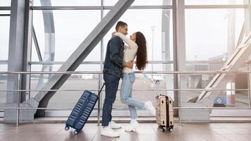 Young Middle Eastern Couple Embracing Near Window At Airport Terminal, Happy Arab Spouses With Suitcases Waiting For Flight Boarding, Ready For Honeymoon Travel, Side View With Copy Space photo