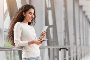 Portrait Of Beautiful Young Woman Using Smartphone While Waiting At Airport, Happy Smiling Middle Eastern Lady Browsing Internet On Mobile Phone While Standing With Luggage At Terminal, Copy Space photo
