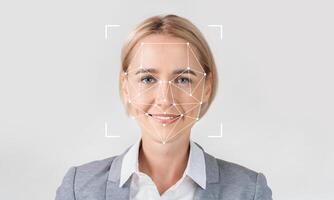 A professional woman smiles while facial recognition technology analyzes her features. She stands against a plain background, highlighting the tech's identification capabilities. photo