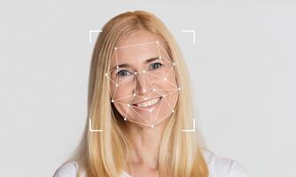 A smiling woman with long blonde hair is featured against an empty background. Facial recognition technology is overlayed on her face, highlighting key facial features and points. photo