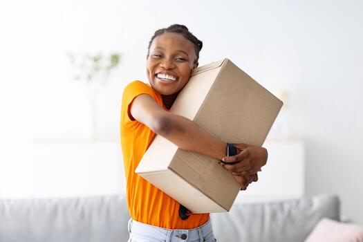 alegre negro mujer abrazando caja de cartón parcela, recepción deseado entrega, consiguiendo en línea orden a hogar. alegre africano americano dama satisfecho con su Internet compra, abrazando paquete foto