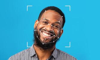 A man with a beard smiles brightly against a solid blue background. Facial recognition technology is overlayed on his face, displaying points of identification for analysis. photo