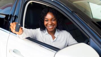 Buying New Car. Happy African American Woman Showing Keys Of Her Automobile Out Of Window, Cheerful Black Female Driver Enjoying Using Auto Rental Service, Smiling And Looking At Camera, Closeup photo
