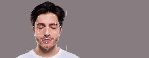 Man with closed eyes demonstrates facial recognition technology, featuring geometric mappings on his face. The setting provides a blank gray backdrop for focus on the subject. photo