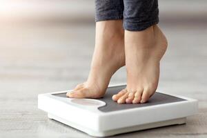 Closeup of young Indian woman standing on scales, measuring her weight indoors. Unrecognizable millennial lady checking result of her slimming process, cropped view of feet photo