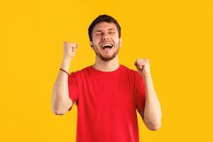 Yes, Great News. Portrait of overjoyed guy screaming and shaking clenched fists raised up in the air, isolated over blue studio background. Excited man cheering and shouting, celebrating triumph photo