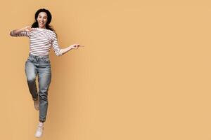 Cool Offer. Excited Joyful Arab Couple Jumping And Pointing In The Middle, Happy Cheerful Middle Eastern Man And Woman Showing Copy Space For Advertisement On Yellow Background, Full Length, Panorama photo