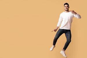 Cool Offer. Excited Joyful Arab Couple Jumping And Pointing In The Middle, Happy Cheerful Middle Eastern Man And Woman Showing Copy Space For Advertisement On Yellow Background, Full Length, Panorama photo