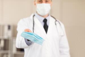 Be Safe Concept. Close up of male doctor or scientist wearing and holding protective facial mask, showing it to camera photo