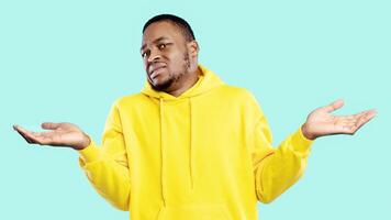 Disgusted African American Guy Shrugging Shoulders Looking At Camera And Disapproving Something Posing Over Blue Background. Studio Shot. Negative Emotions. I Don't Know Concept photo