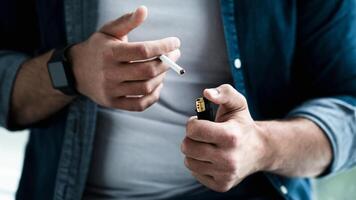 Man smoking cigarette at home. Addiction to nicotine, mental, problems and troubles, bad habit and worry. Sad unhappy millennial european guy lights cigarette, cropped, close up, empty space photo