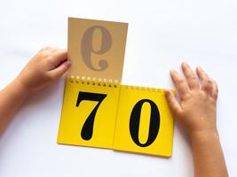 Childs hands flip through yellow pages with numbers. Displaying number 70 on white background photo