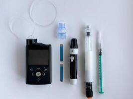 Diabetes management tools, insulin pump, glucometer, and injection supplies on white surface photo