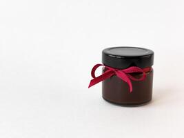 Elegant jar of chocolate spread tied with red ribbon on white background photo
