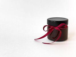 Elegant black jar with red ribbon on minimalist white background photo