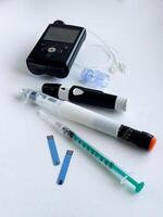 Diabetes management tools, insulin pump, pen, syringe, and test strips on white background photo