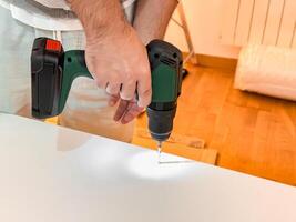 Male adult using cordless drill to assemble furniture in a home setting photo