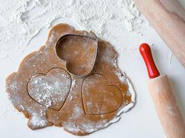 Heart shaped cookie dough with cutters and rolling pin on floured surface photo