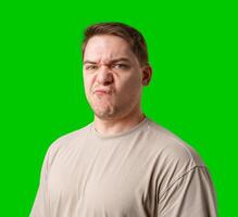 Young man making a disgusted expression while standing against a bright green background photo