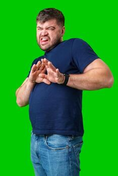 A man with a serious expression holds up both hands in a stopping gesture against a bright green background photo