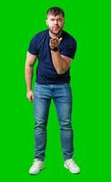 A man blowing a kiss while standing against a bright green backdrop in a casual outfit photo