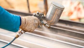Construction worker painting metal structure surface coating with a spray gun at construction site. Metal corrosion and rust protection. Industrial precision. Protective coating to a metal structure. photo