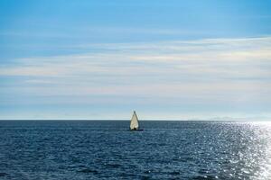 Small sailboat in backlight sailing in the ocean photo