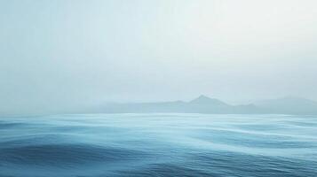 Calm ocean waves gently rolling towards a misty mountain range, creating a tranquil and minimalist seascape photo
