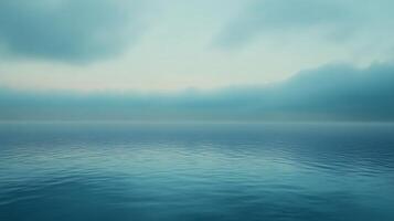 Calm ocean water reflecting a cloudy sky during a misty sunrise, creating a serene and tranquil atmosphere photo