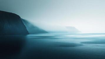 Low fog covering a calm ocean with cliffs in the background during a misty dusk photo