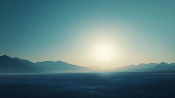 Sunlight illuminates a vast, empty landscape with a mountain range in the background, creating a serene and minimalist scene with teal toned sky photo