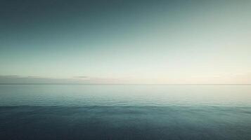 Tranquil ocean surface reflecting the soft pastel hues of the sky at dawn, creating a minimalist and serene seascape photo