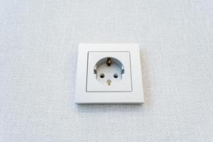 A rectangular metal wall socket blending in with the white wall photo