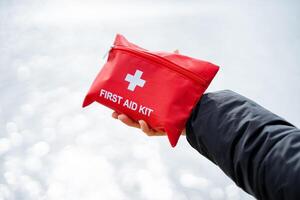 In the image, a person is holding a red first aid kit, prepared for emergencies. Keywords include glove, sleeve, gesture, font, flag, event, fashion accessory, travel, thumb, and wrist photo