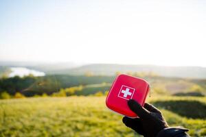 A person holds a red first aid kit in the grassy field photo