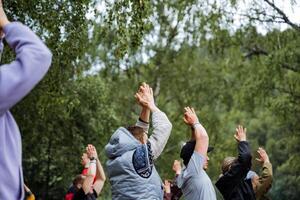 A group of people is seen engaging in outdoor recreational activities in a circle, raising their hands in the air. They seem to be having a good time in a natural setting photo