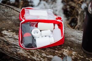 A bright red first aid kit is strategically positioned on a log, effectively showcasing its vibrant color contrasted against the rich and natural wooded backdrop all around it photo